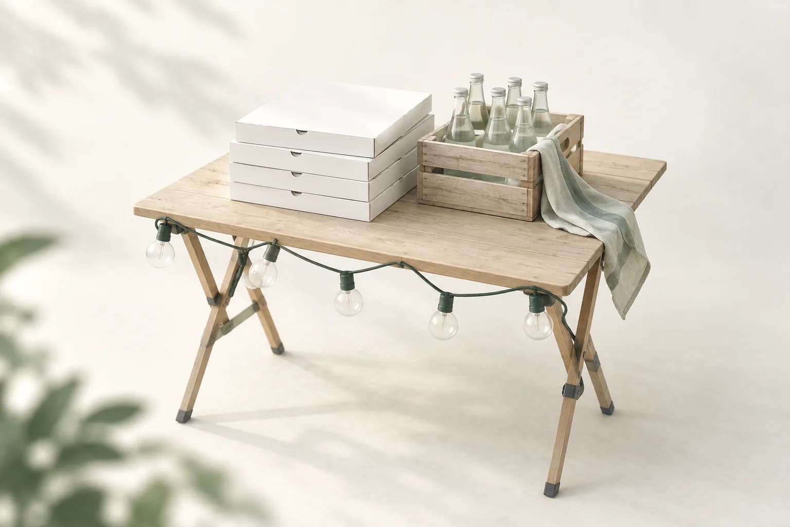 Illustration: Klapptisch aus Holz mit gestapelten Pizzakartons, einer Holzkiste voller Glasflaschen und einem Geschirrtuch, an der Tischkante eine Lichterkette
